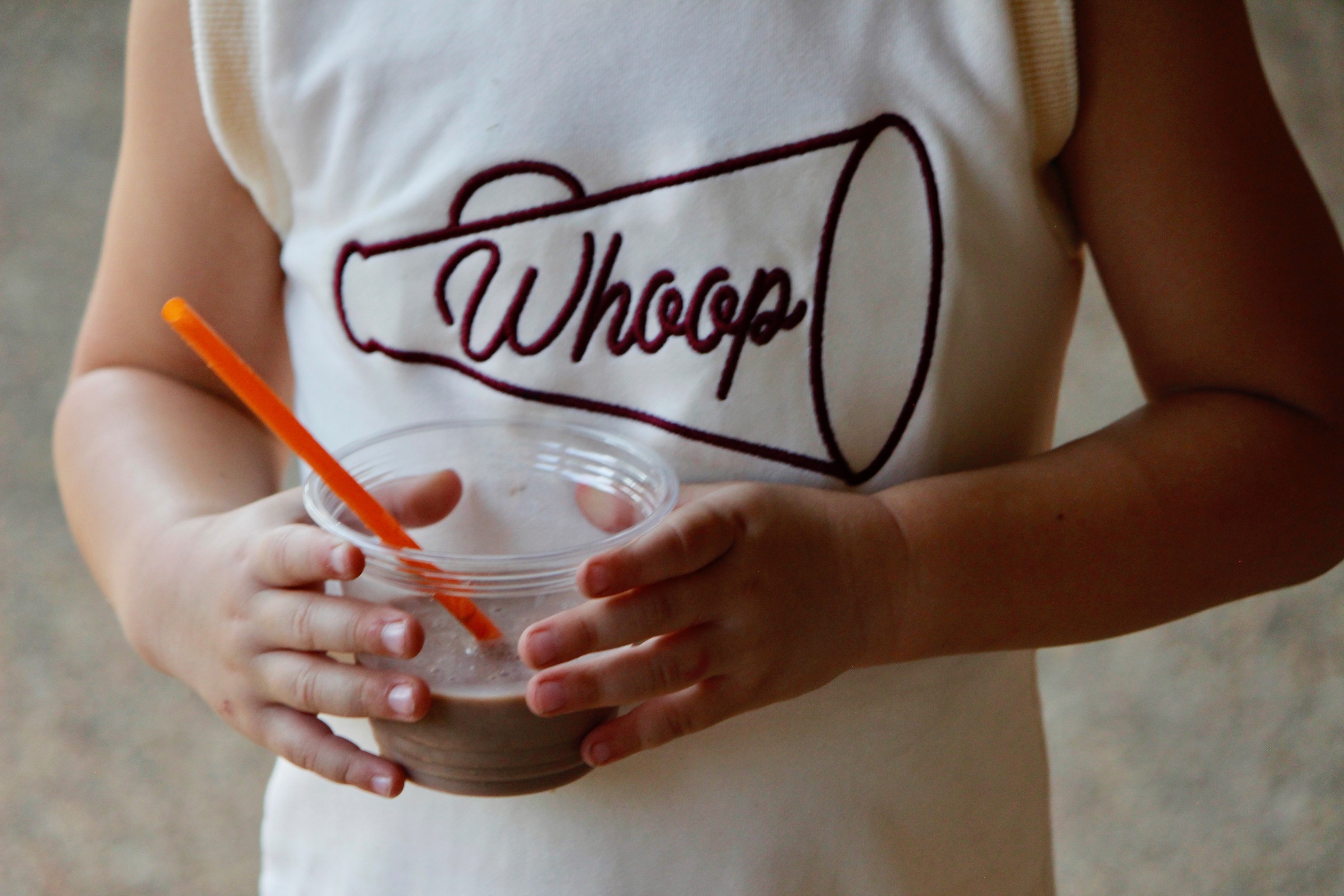 A young Aggie in a Whoop shirt holding a Doc's Slushies cup