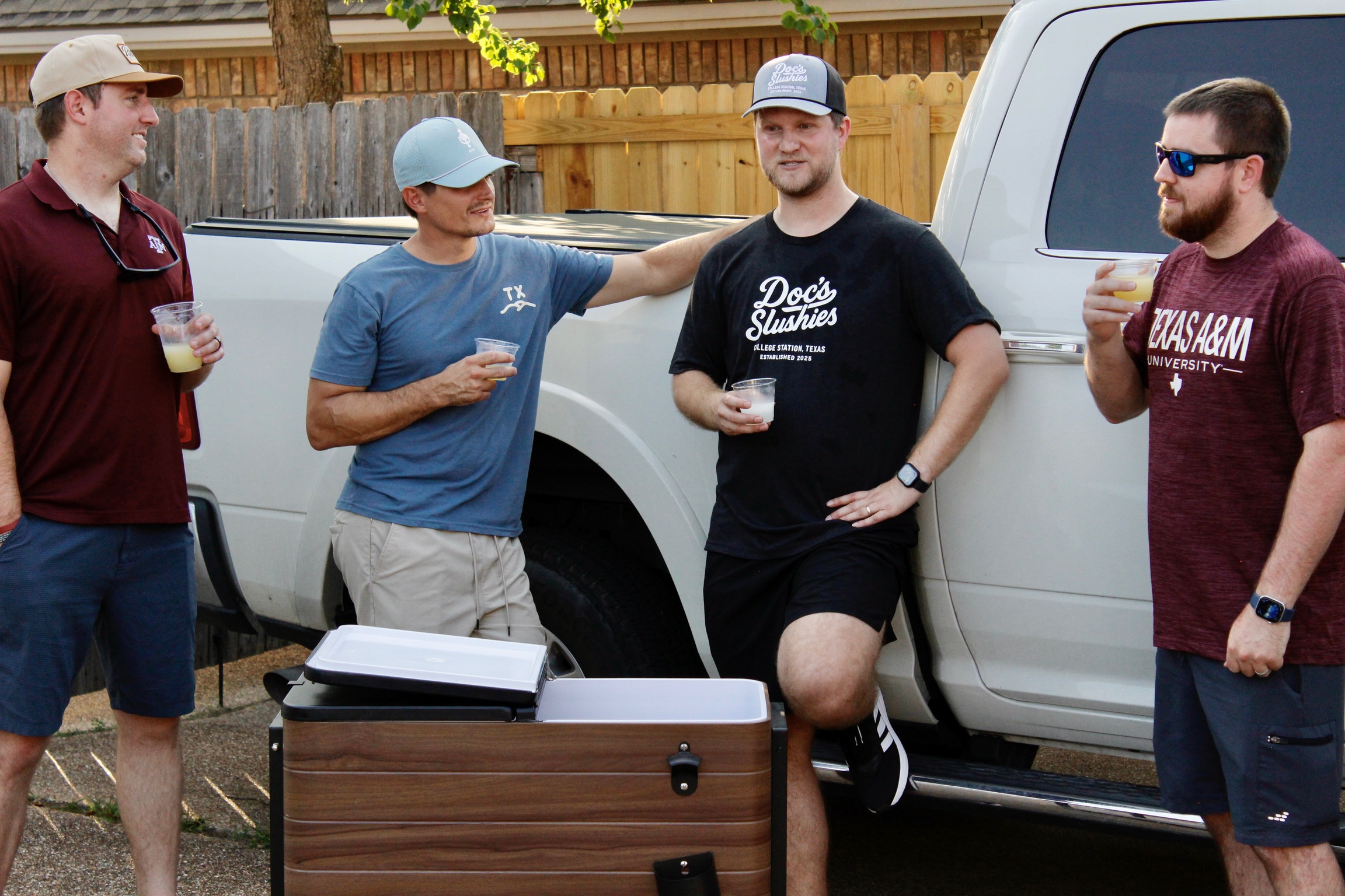 Friends tailgating by a truck with the Doc's Slushies cart and cups in hand
